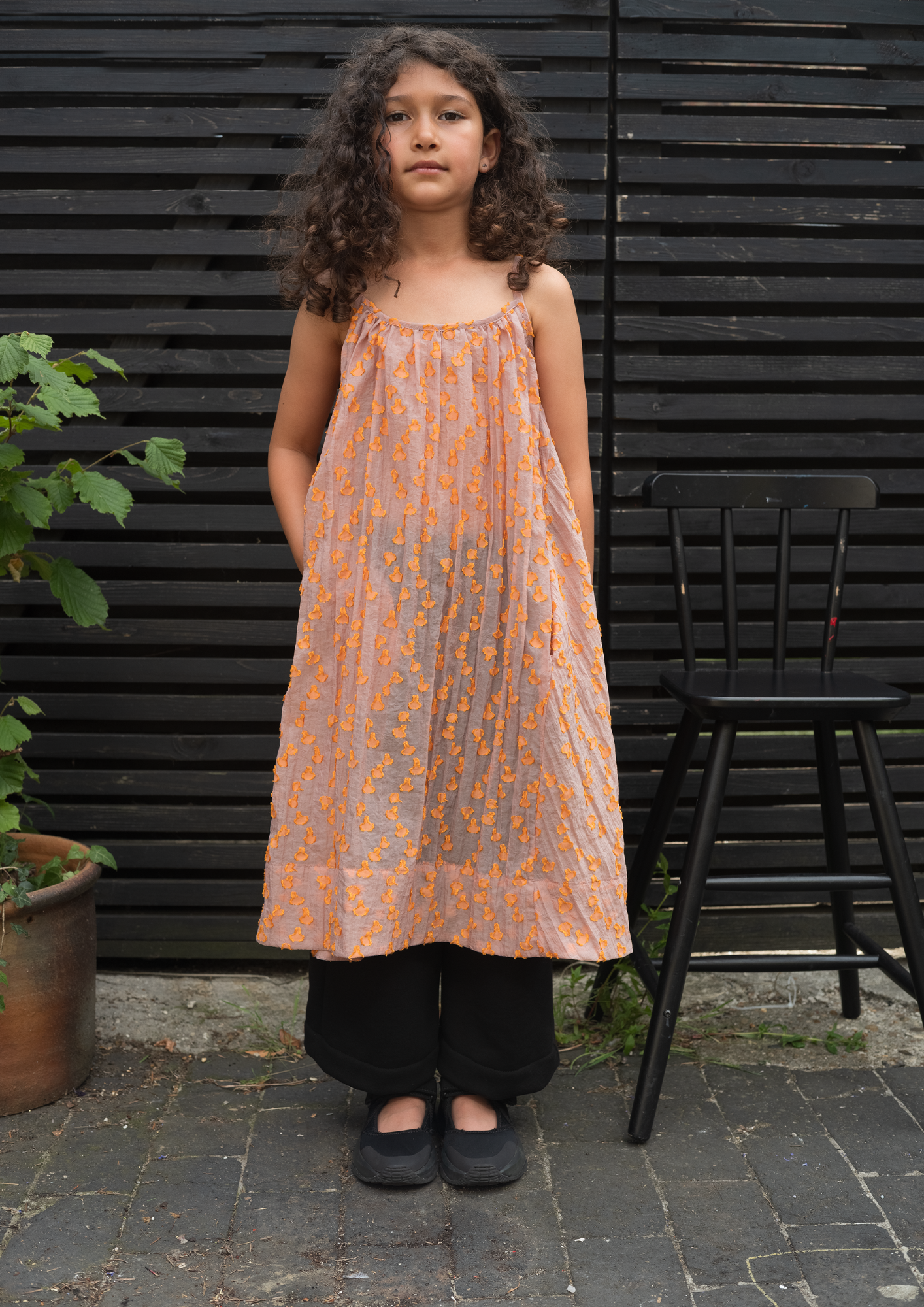 Model wearing cleo sheer dot A-line dress in pink with orange textured dots, modern unisex kidswear
